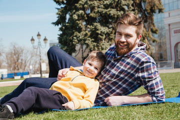 Fototapeta premium Bearded happy father lies outdoors with his son in park
