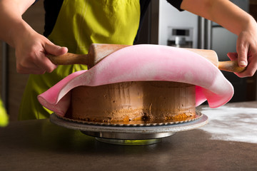 Close up of woman in bakery decorating heart shaped cake with pink royal icing