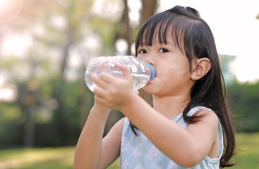 Close Up little girl drinking water from bottle in the park. Portrait outdoor.