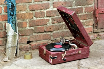 old vintage gramophone player in a red case abandoned outside against the old brick wall