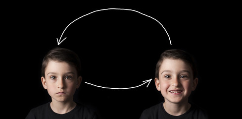 Low key portrait of young boy isolated on black background. Serious face versus smiley face....