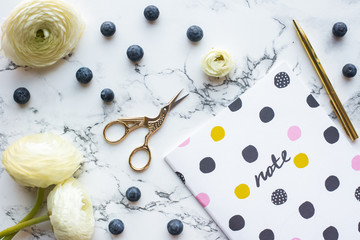 Flat lay, top view of feminine marble table with notes, flowers, pen, blueberries.