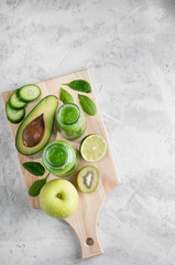 Fresh green smoothies from the green fruits and vegetables on a wooden Board.Concrete grey background.Glass bottle.