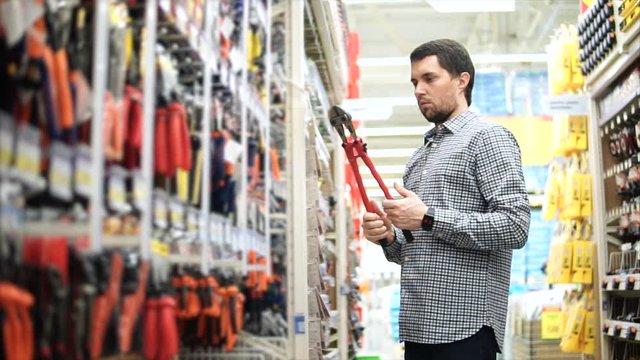 Adult person considers pliers and pliers for metal objects. A man is going to make a purchase in the construction department of a commercial store