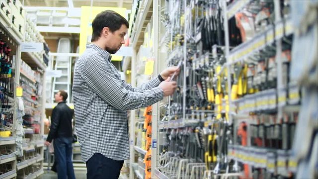Young man looking over the tools and taking a spanner in hardware department store