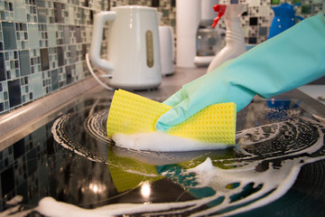 Close-up Of Person Hands Cleaning Induction Stove In Kitchen With Spray Bottle And Sponge