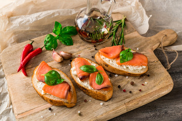 Italian bruschetta set. Sandwiches with cheese and red fish fresh basil, spices, chili peppers, rosemary, garlic. Bottle with olive oil,  on rustic wooden board over dark background,  top view