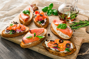 Italian bruschetta set. Varied sandwiches with cheese and red fish, roasted tomatoes, fresh basil, spices, rosemary, garlic, onion, chili pepper. Bottle with olive oil, wooden board,  top view