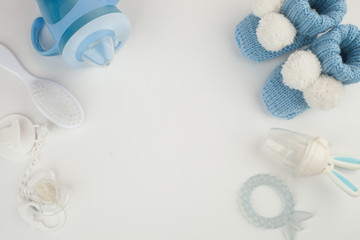 Baby boy accessories background: booties, tiny rod, soother, brush, and toys over white background with copy space; top view. Concept of Infancy and motherhood