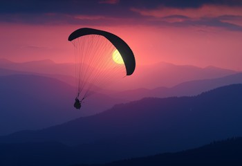 Silhouette of flying paraglide in a light of sunrise