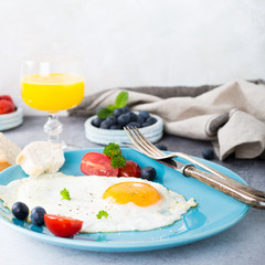 Fried egg on blue plate, tomatoes, blueberries, mint tea and orange juice. Healthy breakfast concept with copy space.