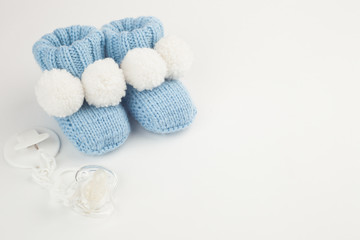 Concept of Infancy and motherhood. knitted newborn baby booties and soother on white background with copy space