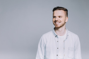 Standing smiling young man with beard in a white shirt