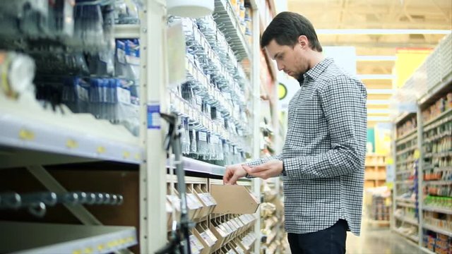 Young man taking several screws from the box in the hardware store. Buying necessary things for repair, construction or home improvements