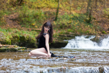 Young girl in a black dress posing on the edge of a waterfall