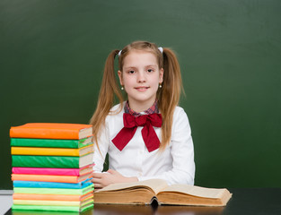 Happy girl with books near empty school green chalkboard