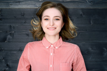 Beautiful young smiling woman in plaid shirt on dark wooden background. Top view