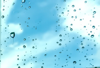 Rain drops, water drops of rain on a window glass with blurred sky clouds