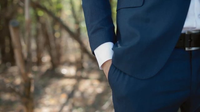 Portrait of young caucasian man outdoor. Groom in blue suit. Young man correct his bow tie  and put his hand to the pocket. Closeup.