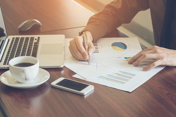 Businessman analyzing graph document with laptop and coffee in office vintage tone.