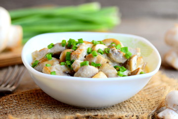 Fried mushrooms slices with sour cream and fresh green onions in a bowl. Healthy vegan meal. Home mushrooms recipe. Fresh mushrooms, green onions, burlap textile on vintage wooden table