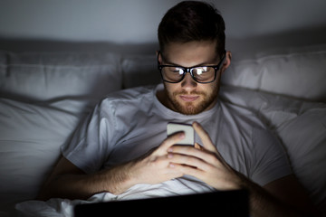 man with laptop and smartphone at night in bed