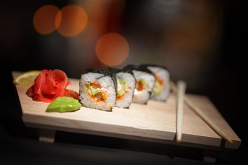Appetizing rolls lie on a wooden plate. Traditional serving. Wasabi, lemon. The atmosphere is warm, cozy restaurant. Creative color.