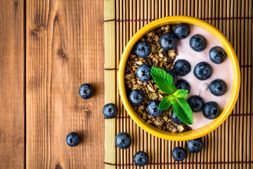 Granola with blueberries and yogurt in yellow bowl on wooden table.