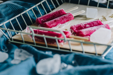 Black currant popsicles decorated with ice cubes. Wooden tray and blue background