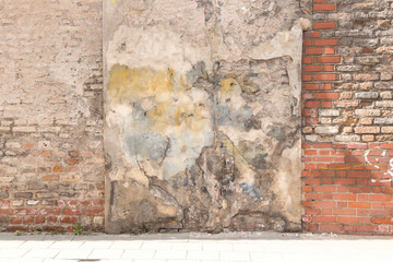 Old weathered vintage brick wall with broken plaster and pavement on the ground. Grungy urban background.