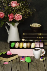 Delicious vibrant Macaroons placed with cup of coffee,beautiful pink roses and books on rustic wooden background 