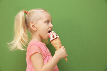 Cute little girl eating ice cream on color background