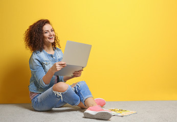 Beautiful young woman using laptop on color wall background