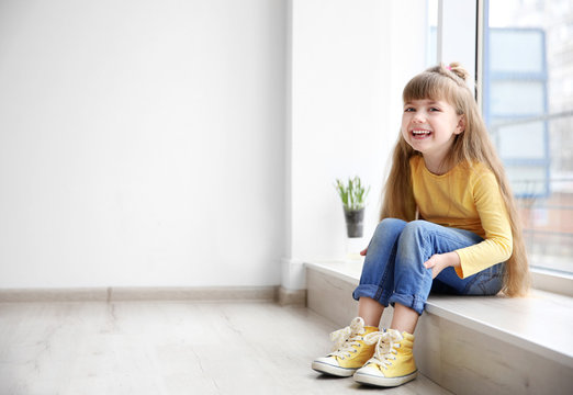 Little fashion girl sitting on window sill in light room