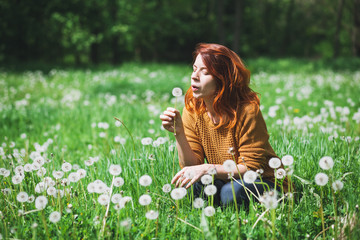 Fototapeta premium Young woman blowing dandelion in the field