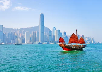 Fototapete Hong Kong Blick auf die Skyline von Hongkong mit einem roten chinesischen Segelboot, das an einem sonnigen Tag am Victoria Harbour vorbeifährt.