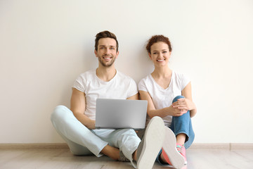 Happy young couple with laptop sitting on floor at home