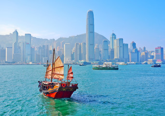 Uitzicht op de skyline van Hong Kong met een rode Chinese zeilboot die op een zonnige dag de Victoria Harbour passeert.