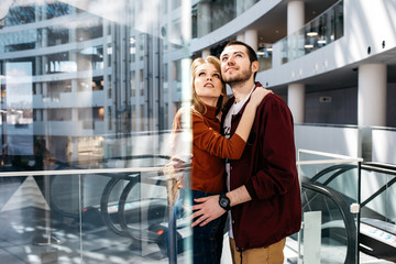 Young and handsome man and woman embrace and look up, stand inside modern business center