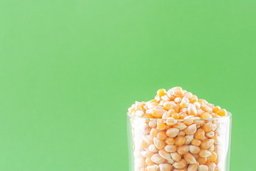 Grains of raw corn in glass on a green background