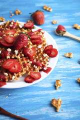 Waffles with strawberry on white plate on blue background.