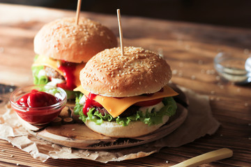 Two handmade burgers with beef, salad and cheese on wooden table.