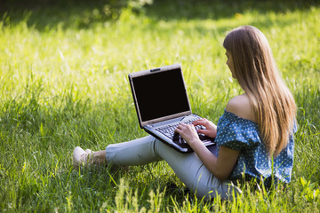 Young attractive woman with a laptop sitting on the grass. Happy face and smile.