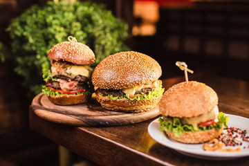Three juicy tasty burger on the white plate on a dark background