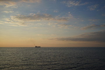Naklejka na ściany i meble a lonely ship on the horizon in the sea at sunset and a cloudy sky
