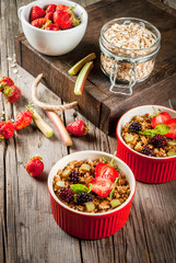 Healthy breakfast. Oatmeal granola crumble with rhubarb, fresh strawberries and blackberries, seeds and ice cream in baked bowls, decorated with mint, on a wooden rustic table in old tray, copy space