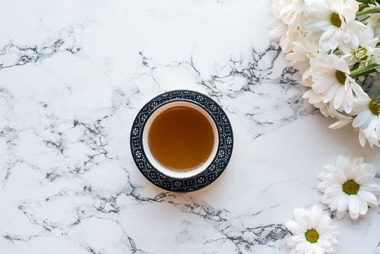 Top view of cup of tea and flowers on white marble background, flat lay
