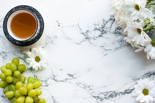 Top view of cup of tea and flowers on white marble background, flat lay