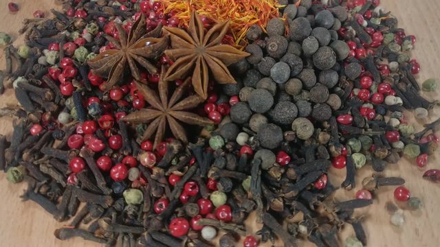 Spices.
Mix of Red, Black, White and Green Hot Peppers, saffron, carnation, star anise is rotating on wooden background 
