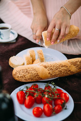 Girl cut baguette on a plate next to cherry tomatoes, white cup of coffee and a basket.
